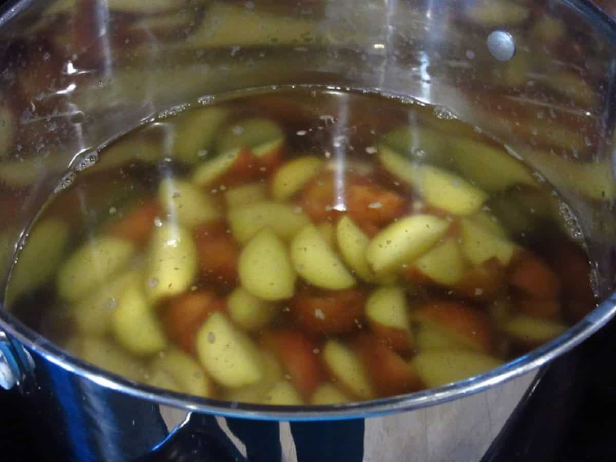 Red potatoes cooking in water on the stovetop.