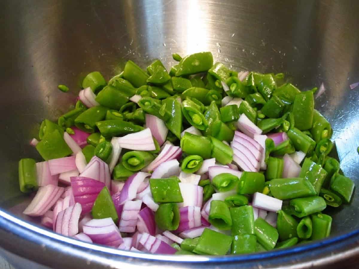 Chopped sugar snap peas and red onion in a stainless steel bowl.