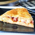 A slice of stuffed double crust Hawaiian pizza on a black plate.