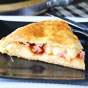 A slice of stuffed double crust Hawaiian pizza on a black plate.