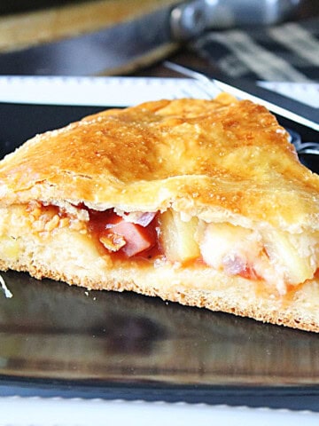 A slice of stuffed double crust Hawaiian pizza on a black plate.