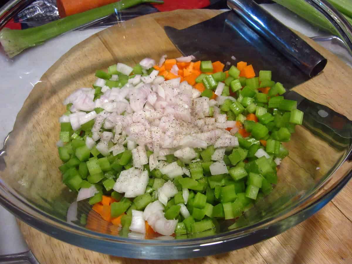 Diced carrots, celery, and shallots in a glass bowl.