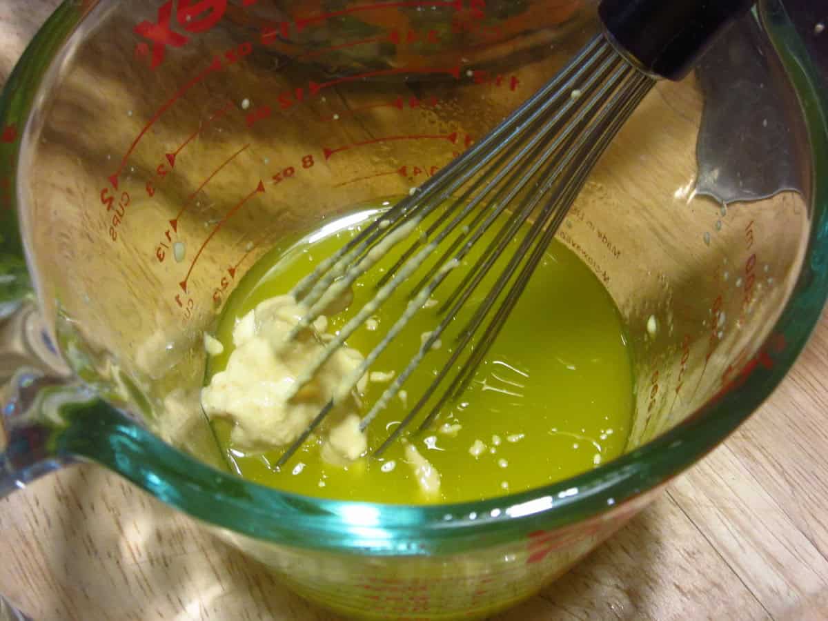 Olive oil and mustard in a glass measuring cup.