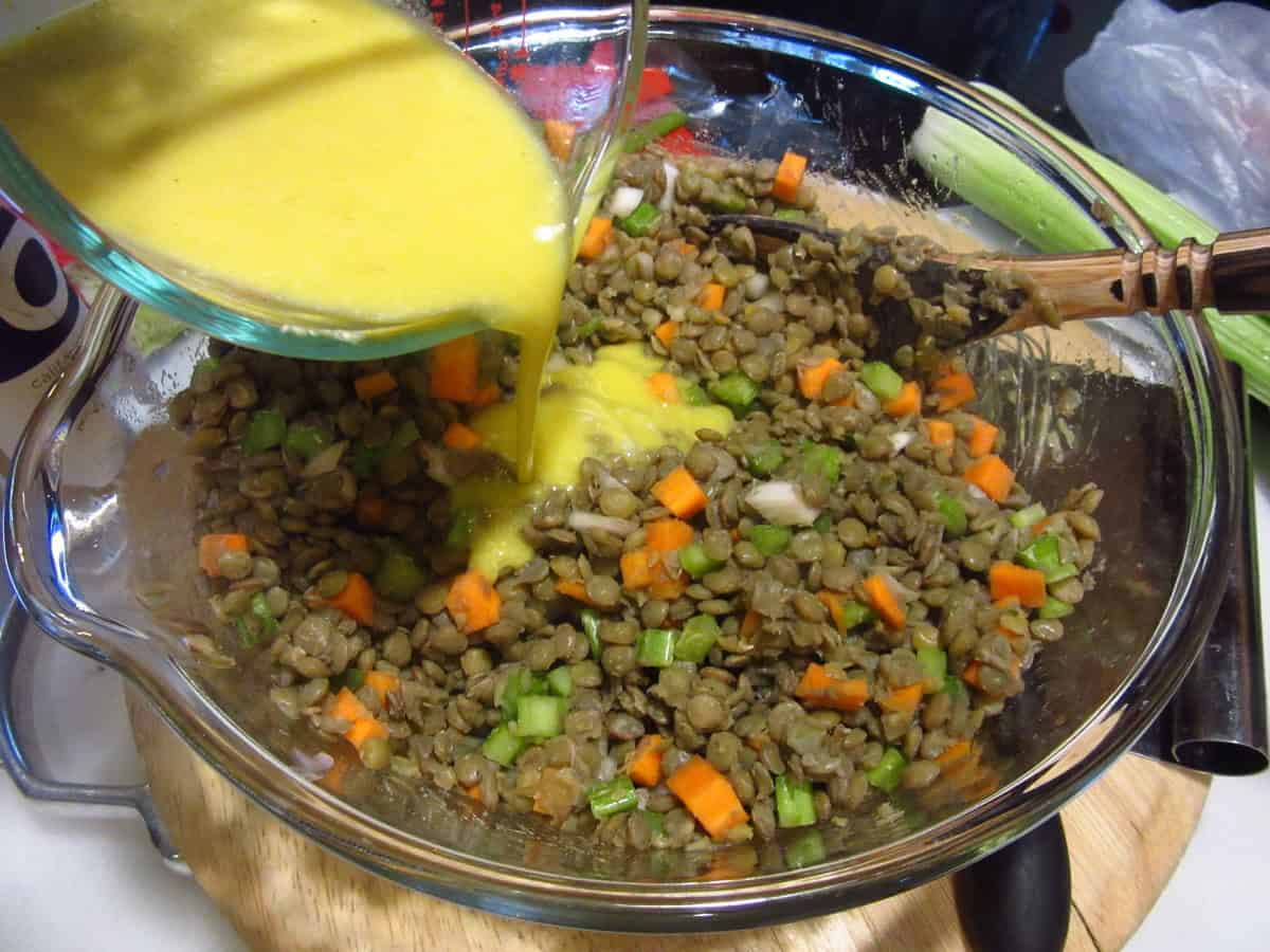 Lemon vinaigrette being poured over a lentil salad in a glass bowl.