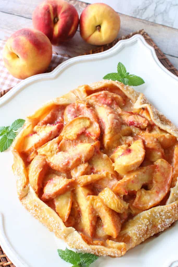A pretty peach crostata garnished with fresh mint on a square white plate.