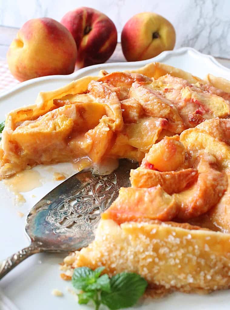 A peach crostata with a slice taken out along with a silver pie server.