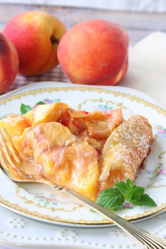 A pretty china plate with a serving of peach crostata and a fork.