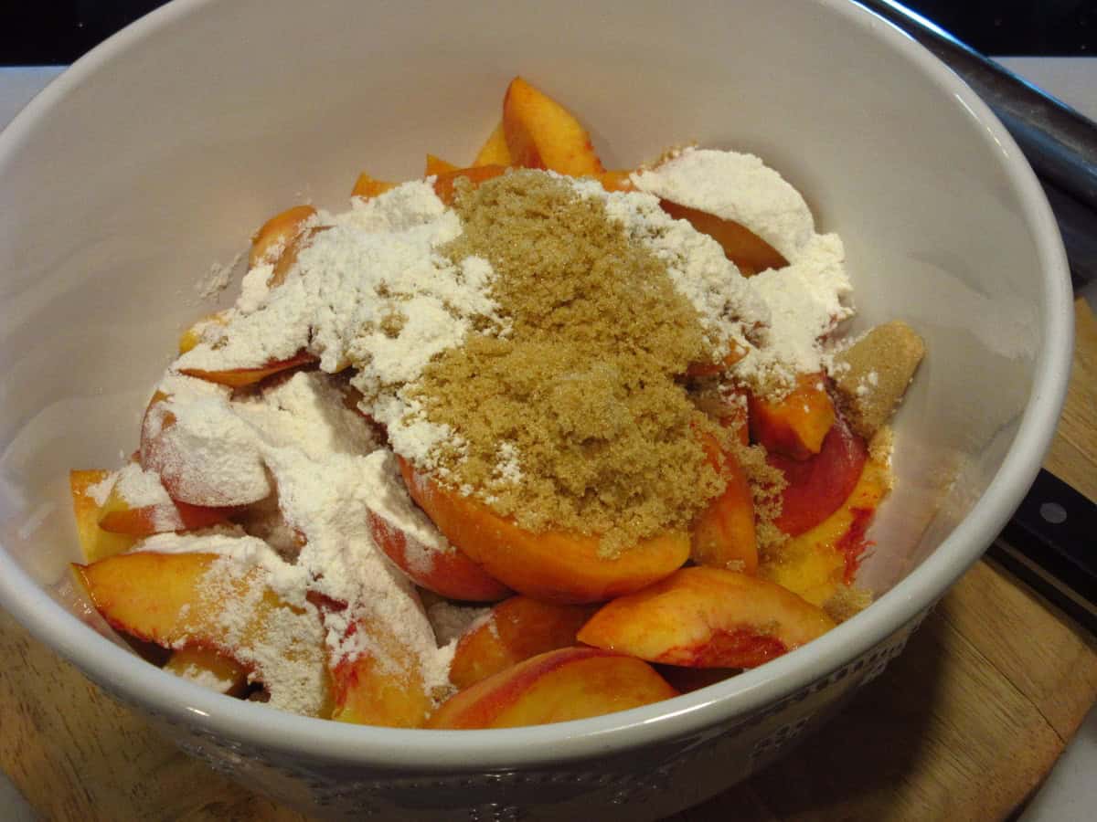 Fresh peaches, flour, and brown sugar in a large white bowl.
