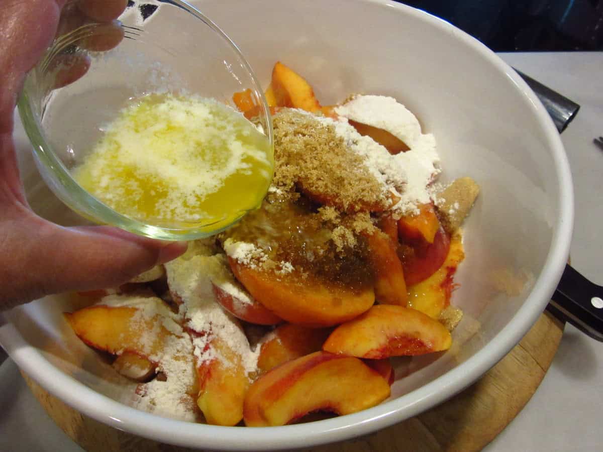 Melted butter being poured into a large bowl with peaches for making a peach crostata.