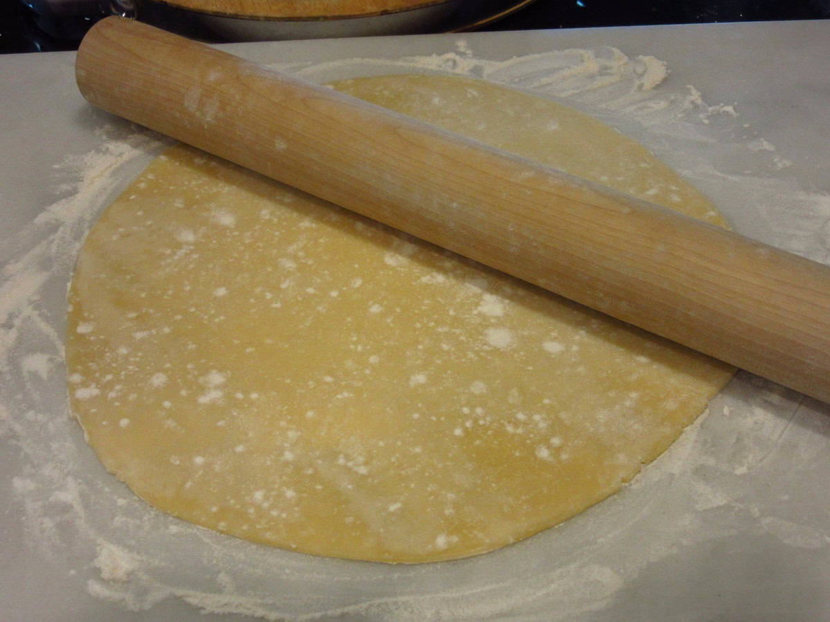 A round pie crust and a rolling pin on a floured countertop.