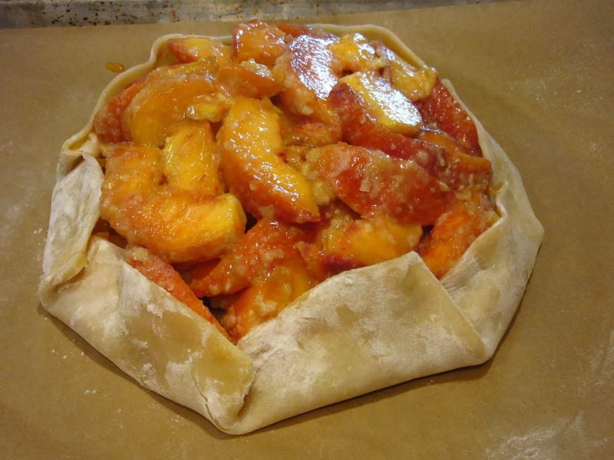 An unbaked peach crostata on a baking sheet before going into the oven.