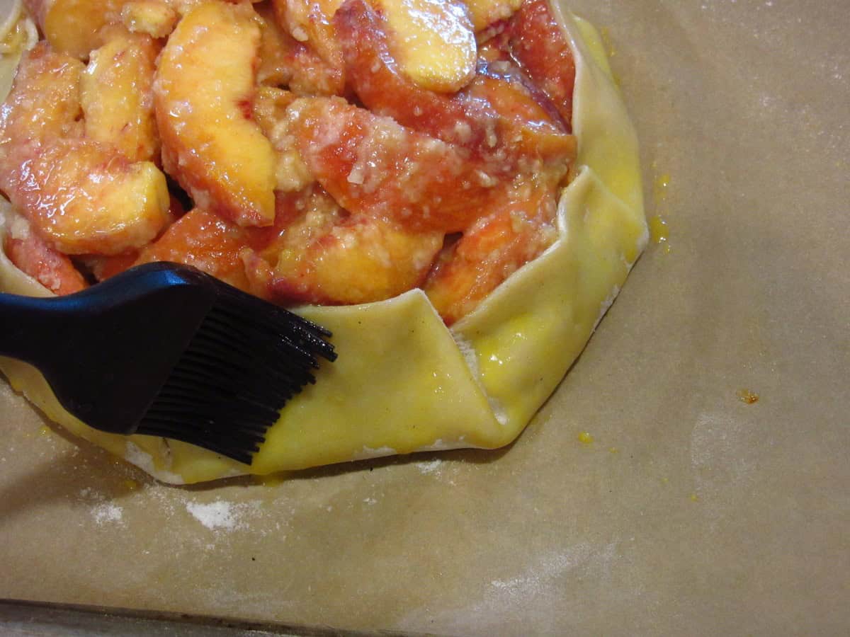 Egg wash being brushed on the pie crust of a crostata.