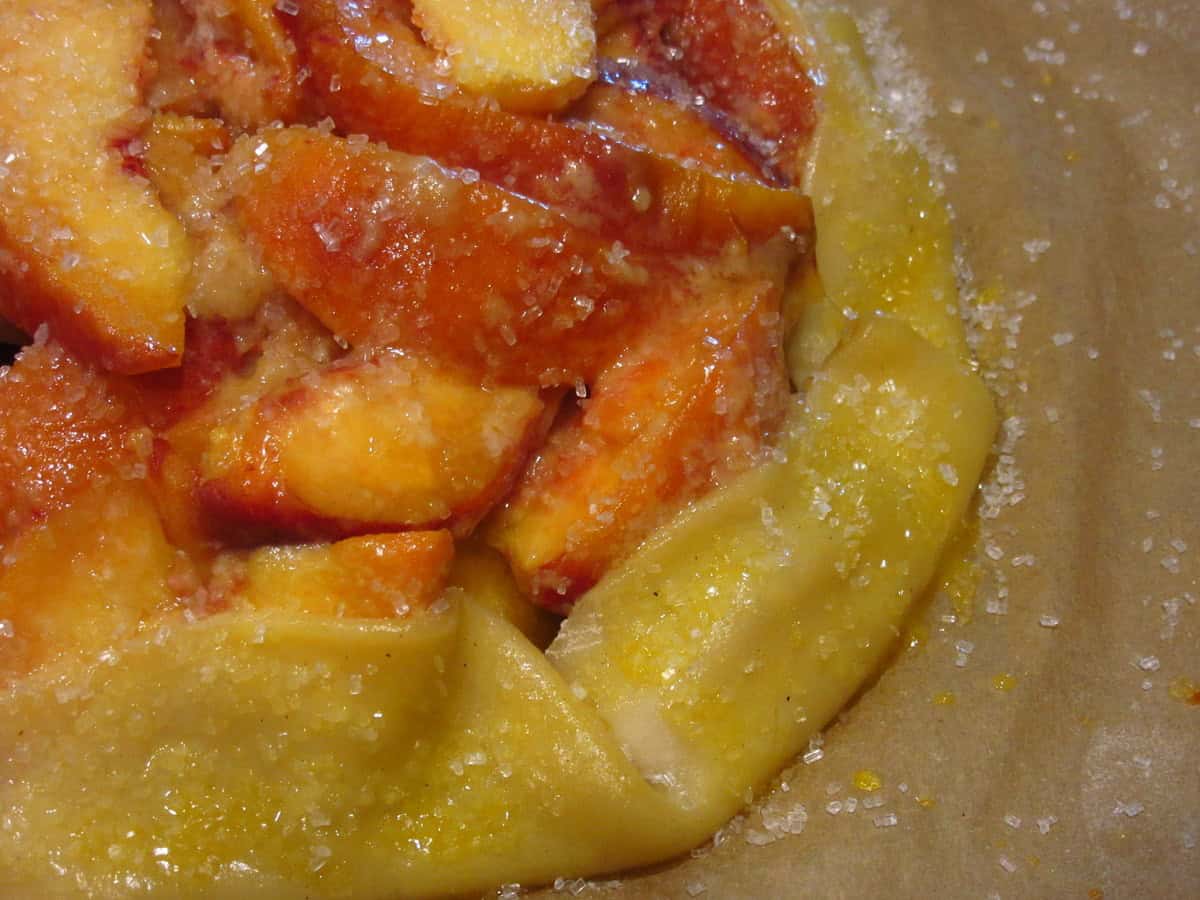 Sanding sugar sprinkled on the unbaked crust of a peach crostata.
