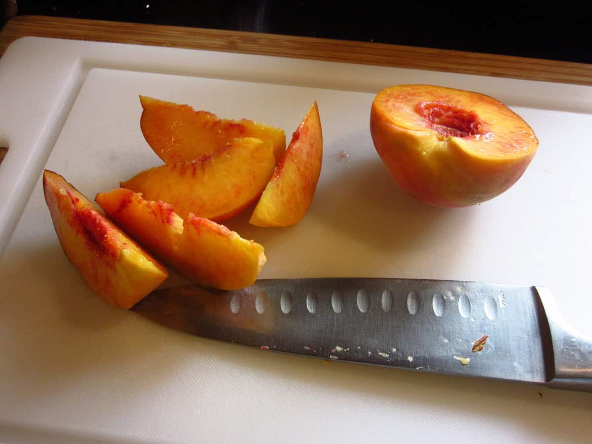 Slices of fresh peach on a cutting board with a knife.