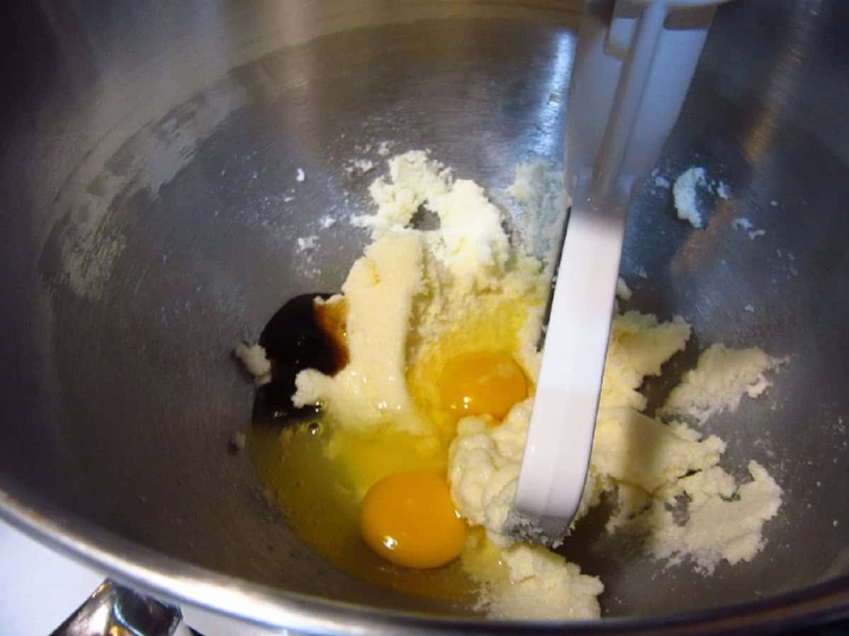 Two eggs, vanilla, and creamed butter in the bowl of a stand mixer.