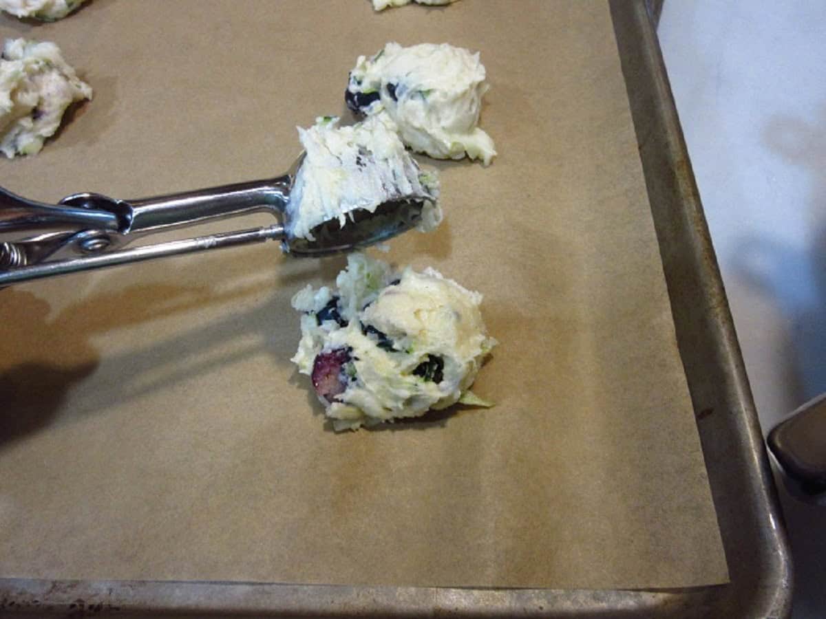 A cookie scoop scooping a dollop of lemon ricotta cookie dough out onto a baking sheet.