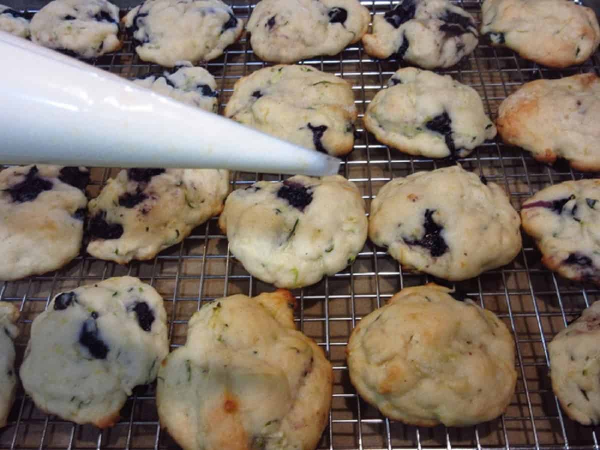A piping tip filled with glaze over a cooling rack filled with lemon ricotta cookies.