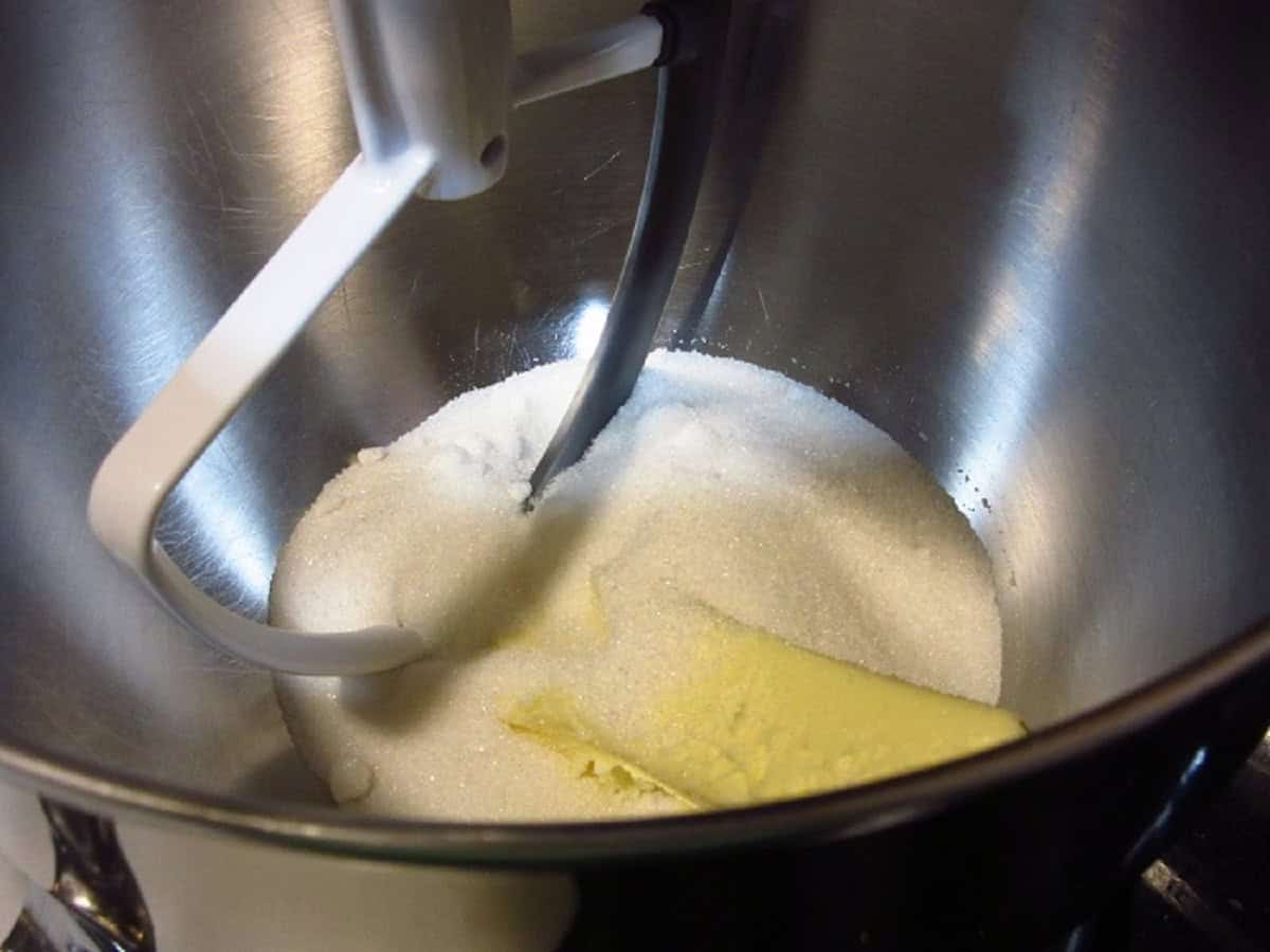 A stick of butter and granulated sugar in the bowl of a stand mixer.