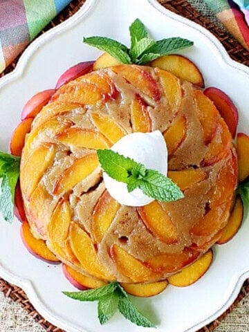 An entire Nectarine Upside Down Cake on a pretty white plate with mint and whipped cream as garnish.