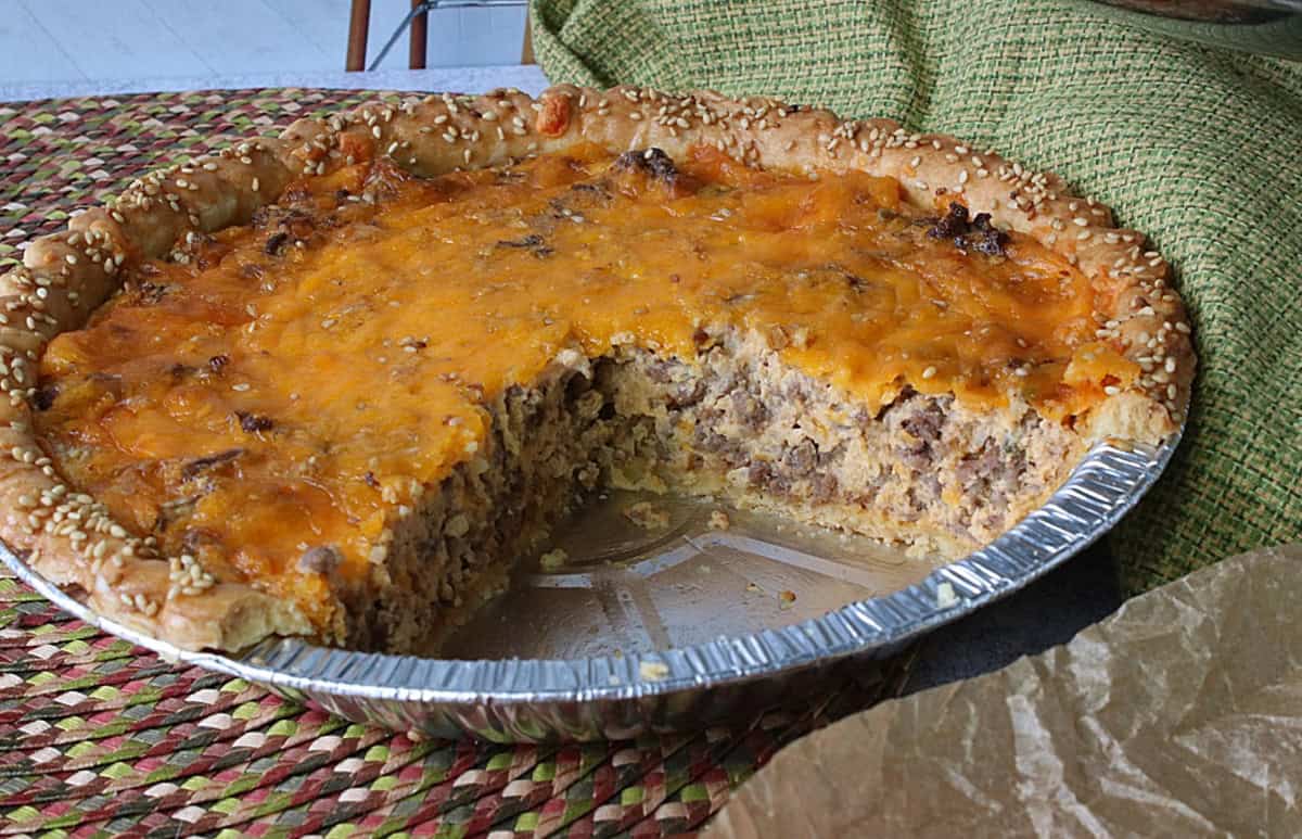 A Big Mac Quiche in a metal pie plate with a few slices taken out.