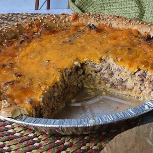 A Big Mac Quiche in a pie tin with a large slice taken out.