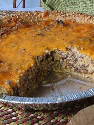 A Big Mac Quiche in a pie tin with a large slice taken out.