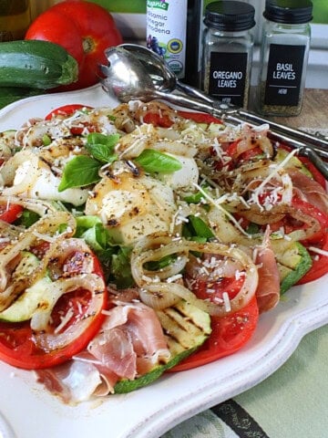 A pretty Caprese salad with zucchini and burrata on a square decorative platter.