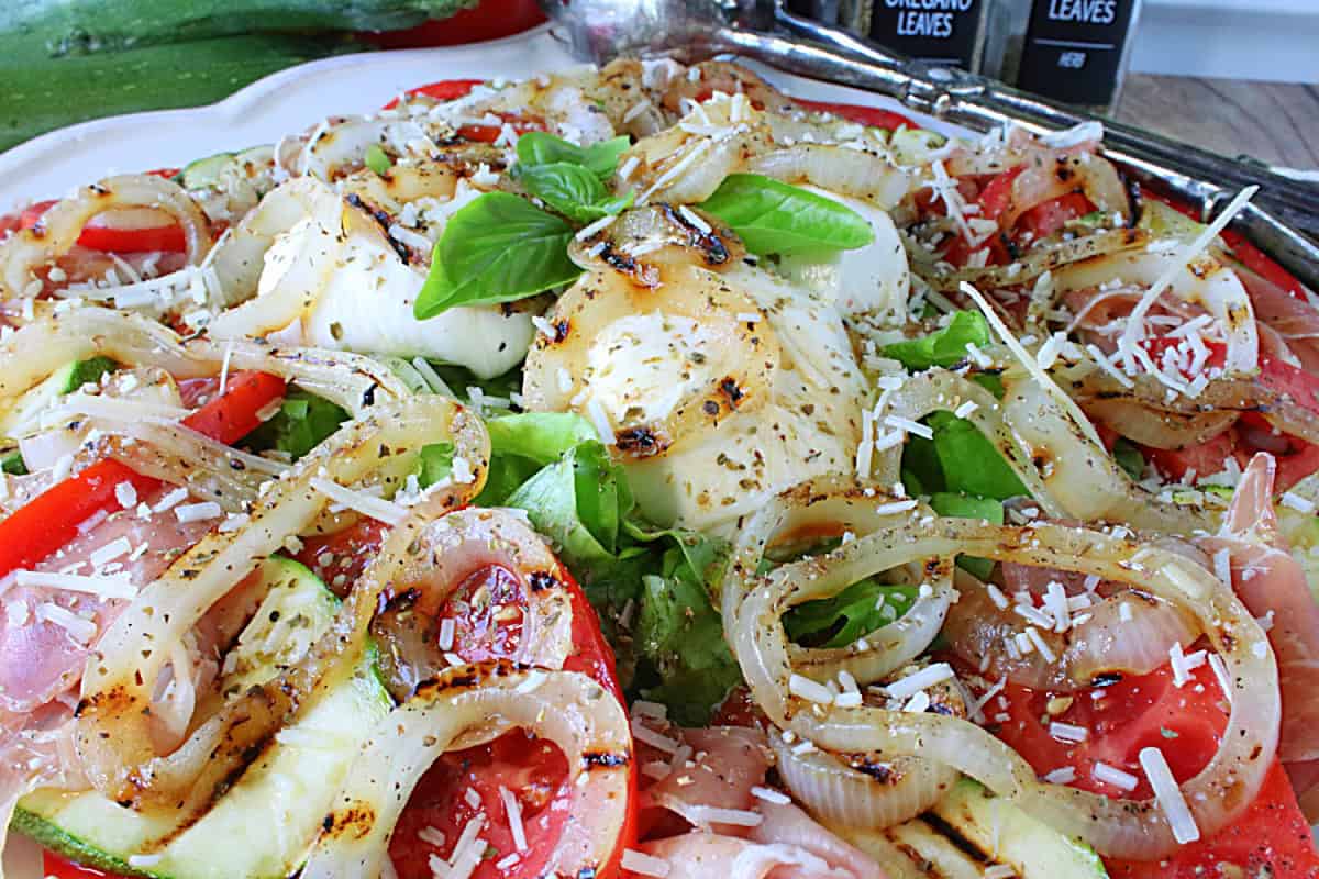 A closeup of burrata cheese on a Caprese Salad with grilled onions and fresh basil.