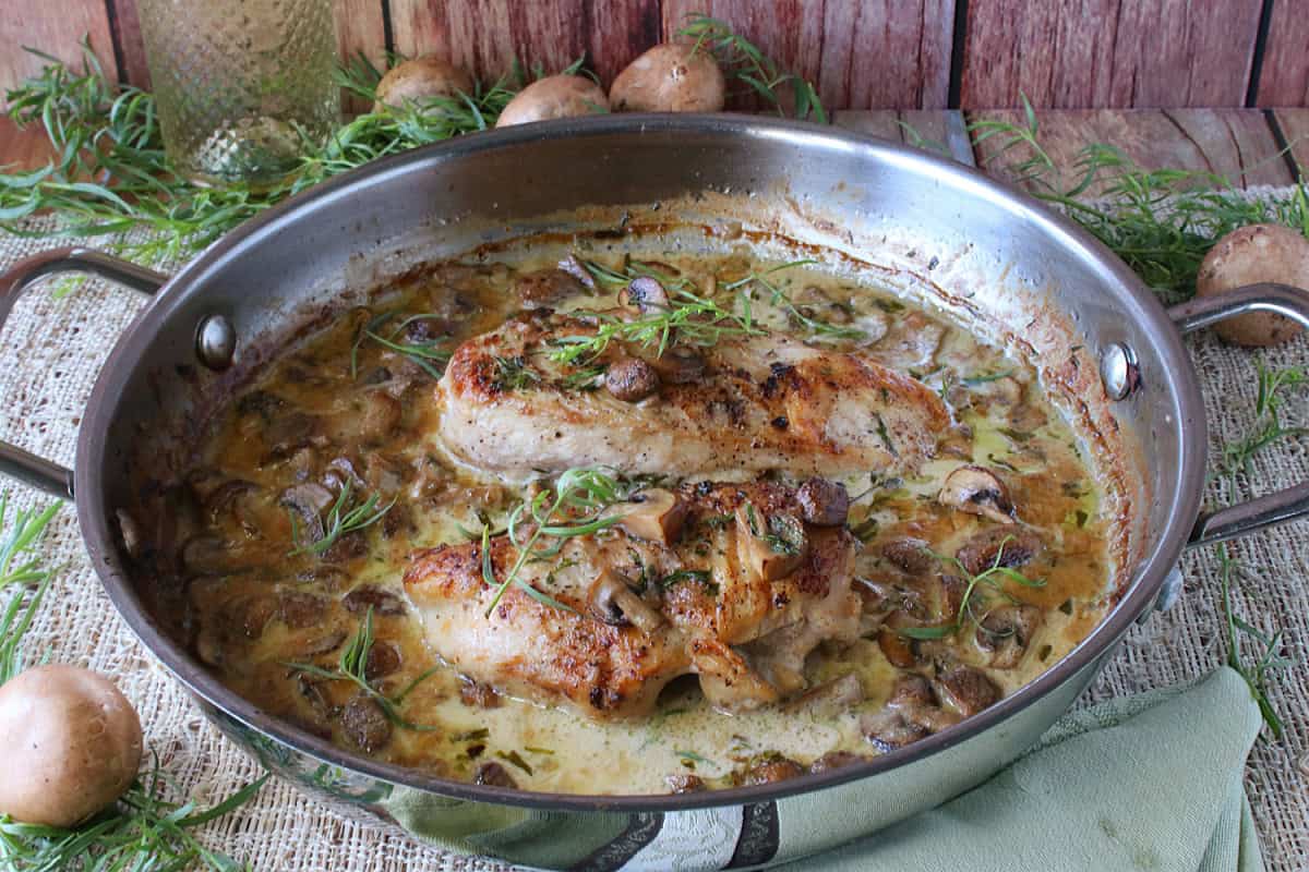 A large silver sauté pan containing Creamy French Tarragon Chicken breasts with mushroom sauce.