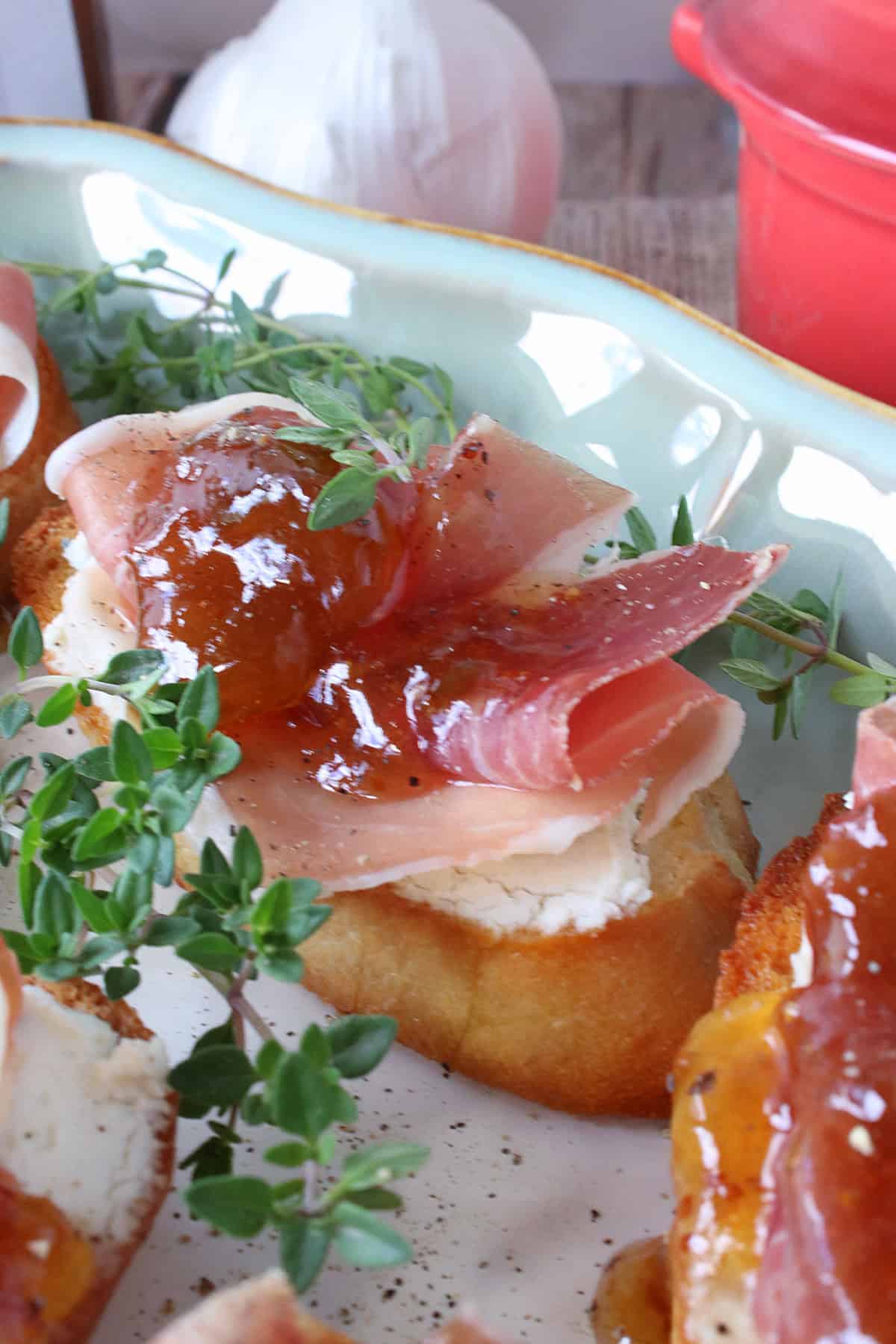 A Fig Jam and Prosciutto Crostini appetizer topped with fresh thyme.