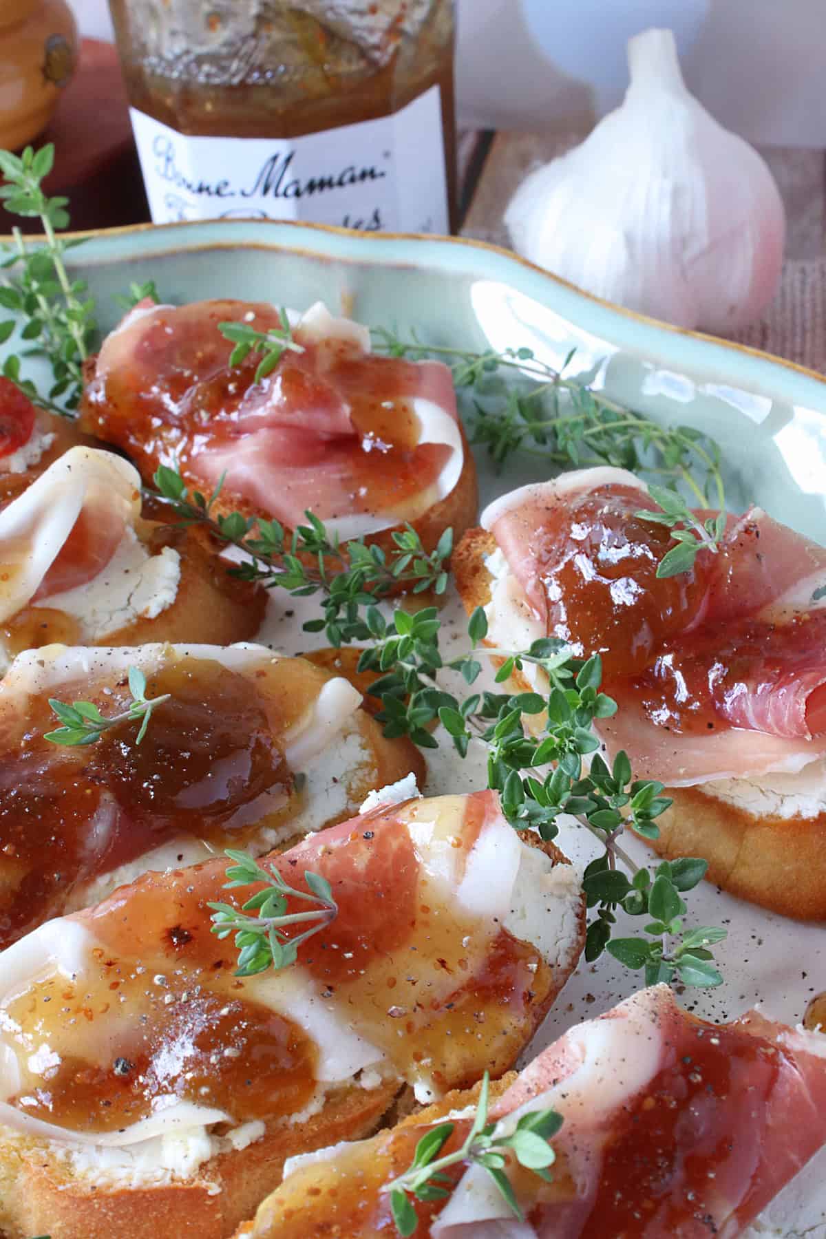 A pretty platter filled with Fig Jam and Prosciutto Crostini topped with freshy thyme and pepper.