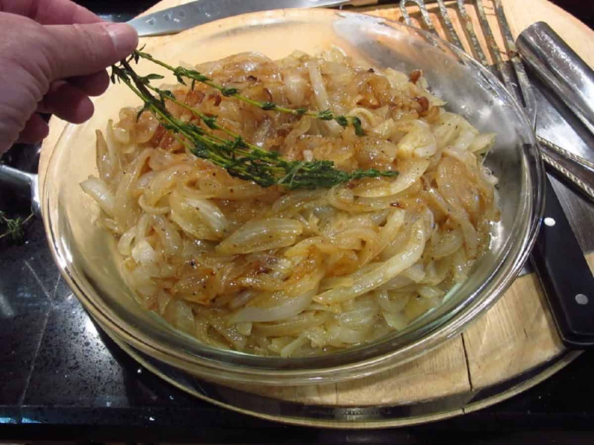 Thyme being taken out of a bowl with caramelized onions.
