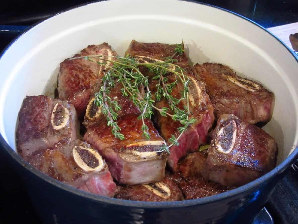 Browned beef short ribs with fresh thyme in a pot on the stove.