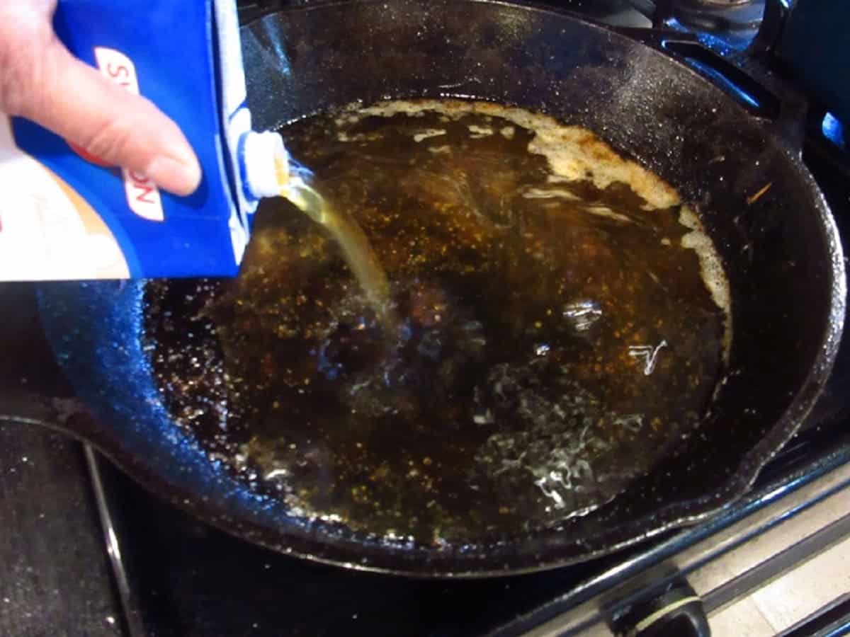 Beef stock being added to a cast iron skillet.
