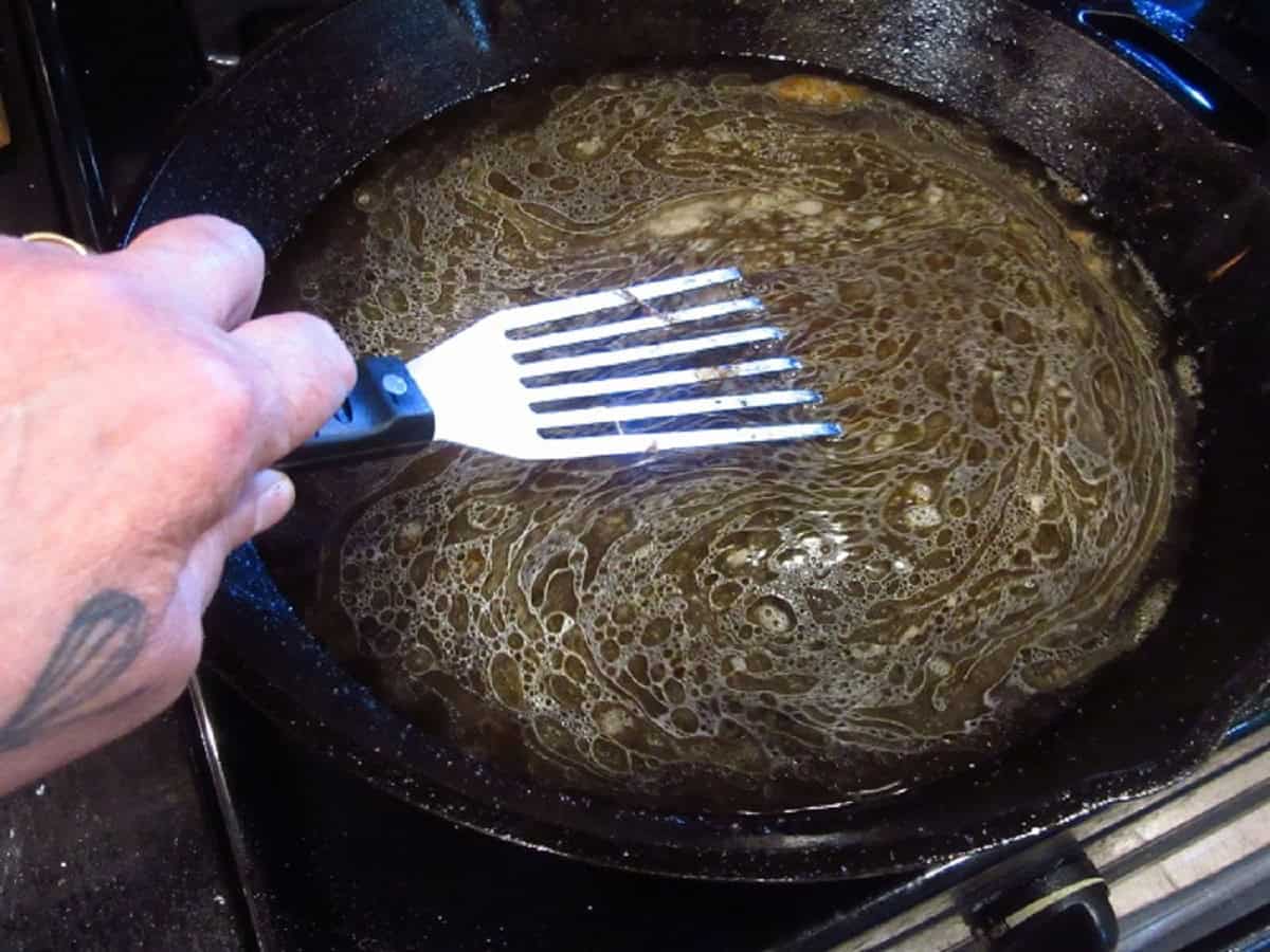 A slotted spatula in a cast iron skillet with beef stock.