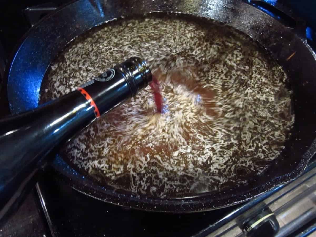 Red wine being added to a cast iron skillet.