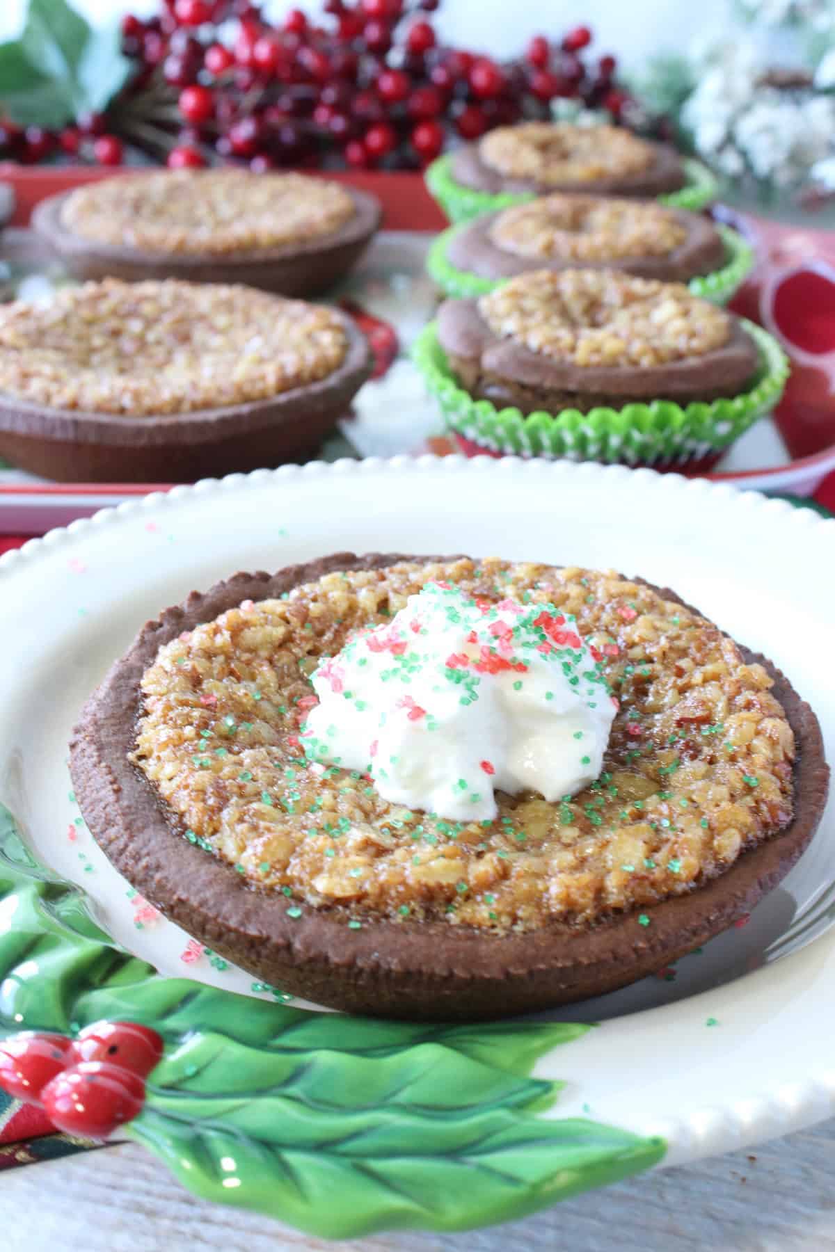A Gingerbread Pecan Pie Tart with whipped cream in the foreground and a bunch of others in the background.