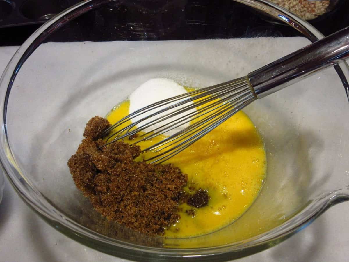 Brown sugar, sugar, and eggs in a glass bowl with a whisk.