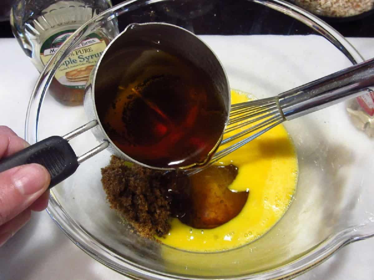 Maple syrup being added to eggs in a glass bowl.