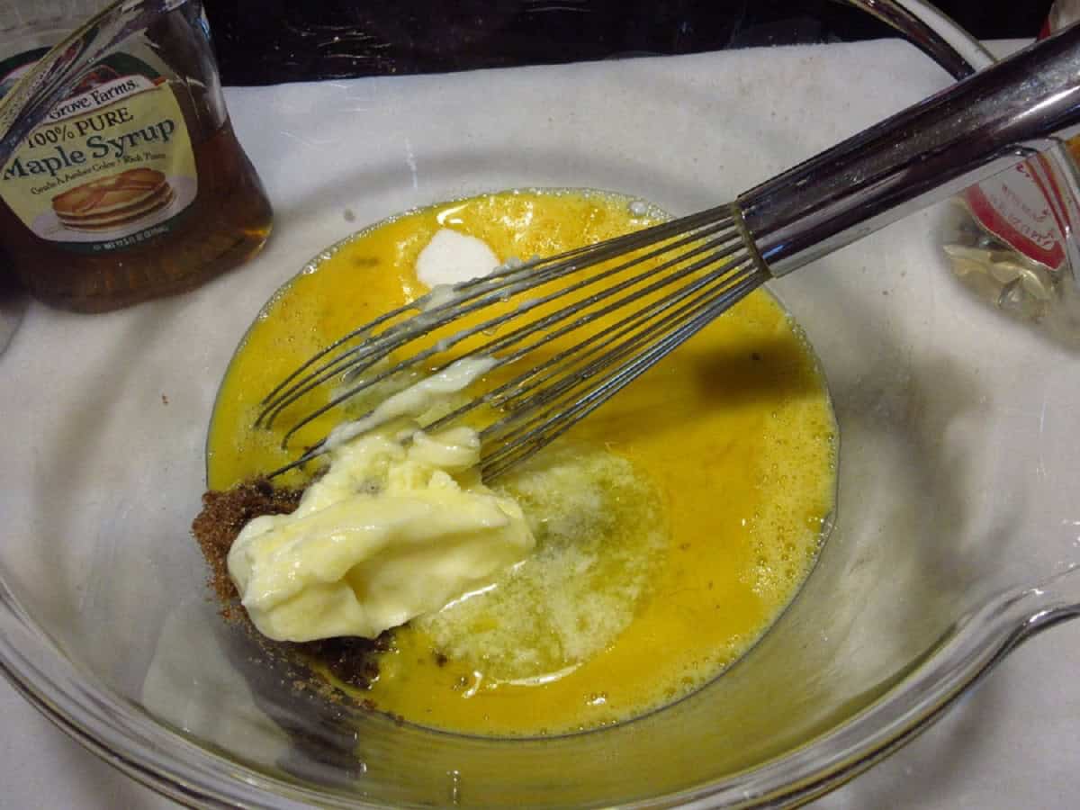 Butter, eggs, and brown sugar in a glass bowl with a whisk.