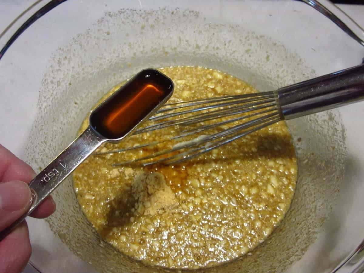 A teaspoon of vanilla extract being added to some pecan pie filling.