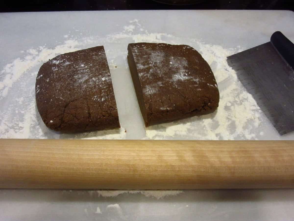 Gingerbread cookie dough cut into two pieces on a floured surface.