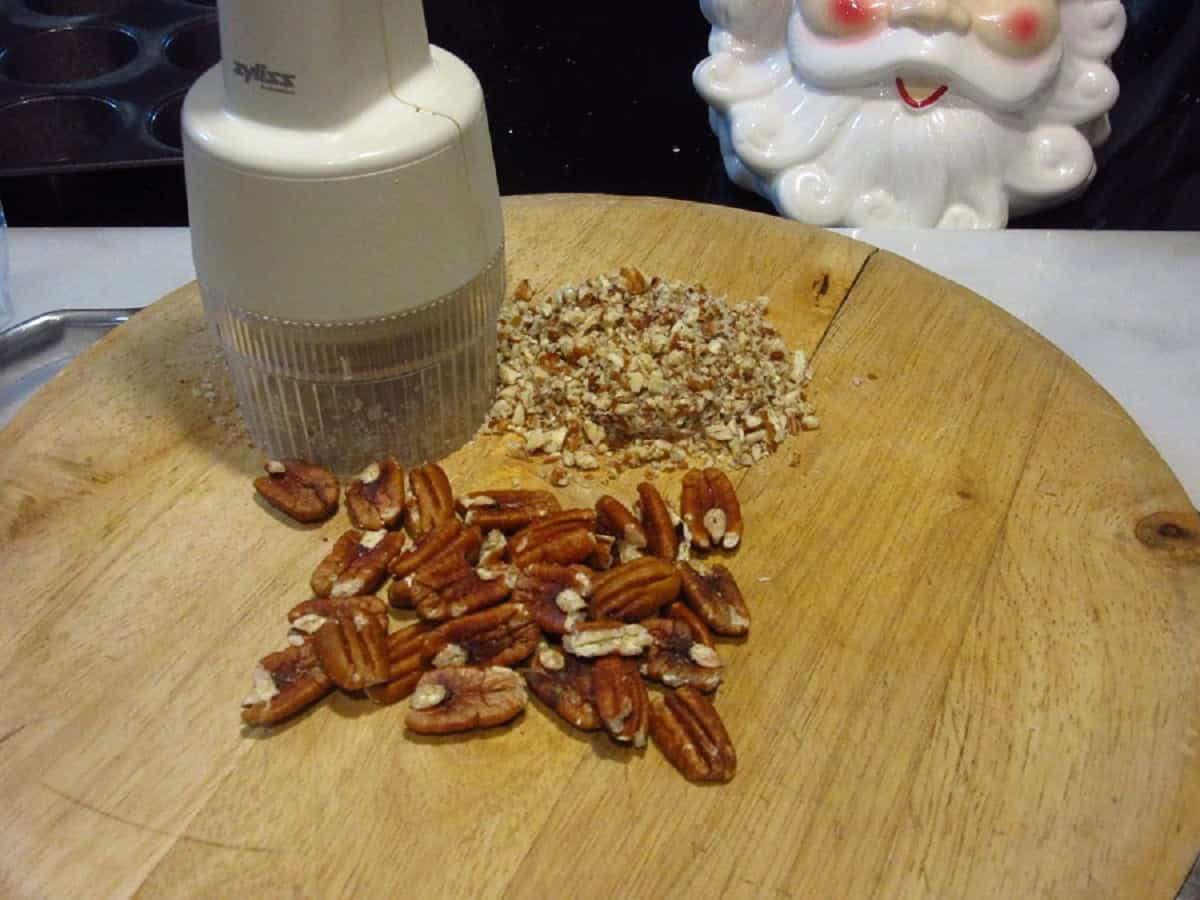 Pecans being chopped on a wooden cutting board.