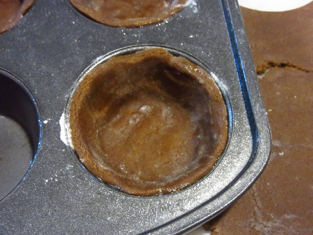 Unbaked gingerbread pie crust pressed into a muffin tin.