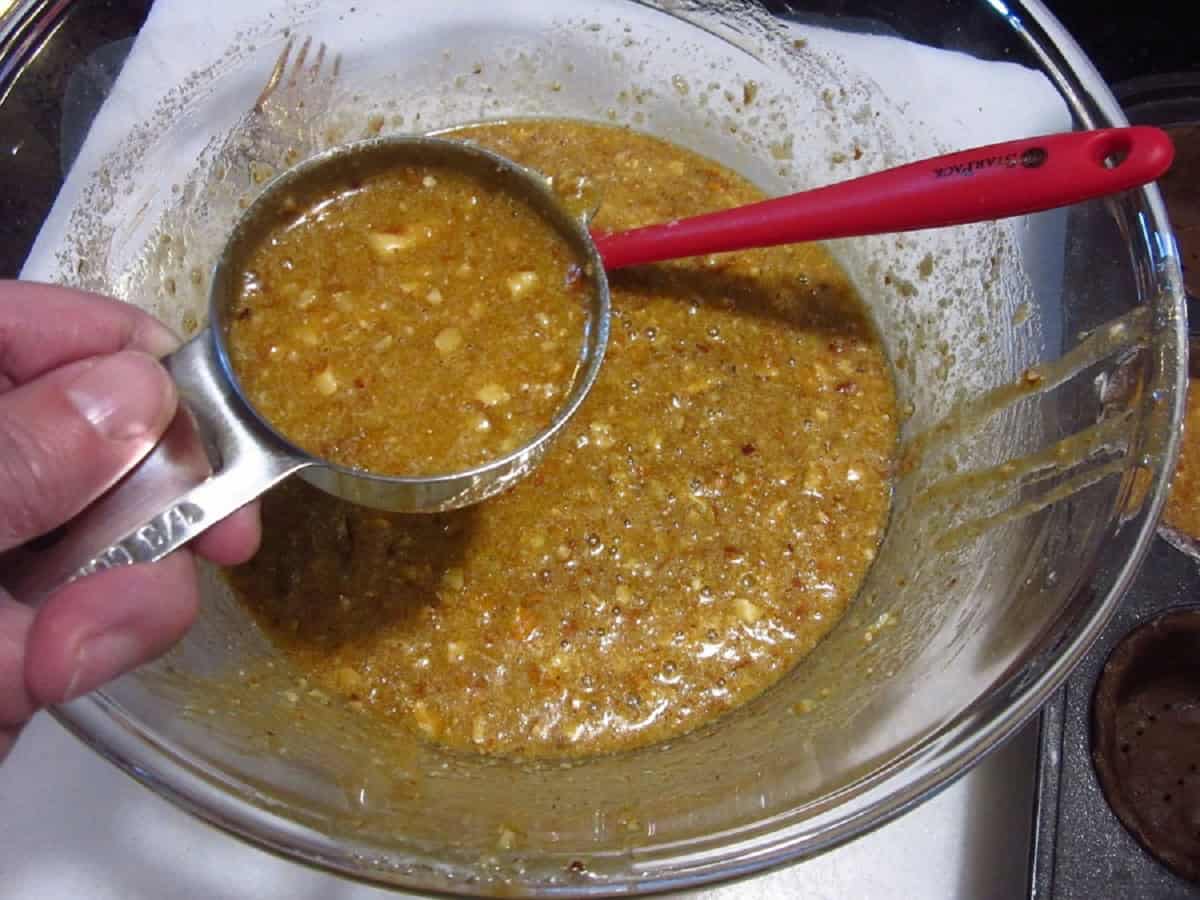 A measuring cup with pecan pie filling over a bowl.
