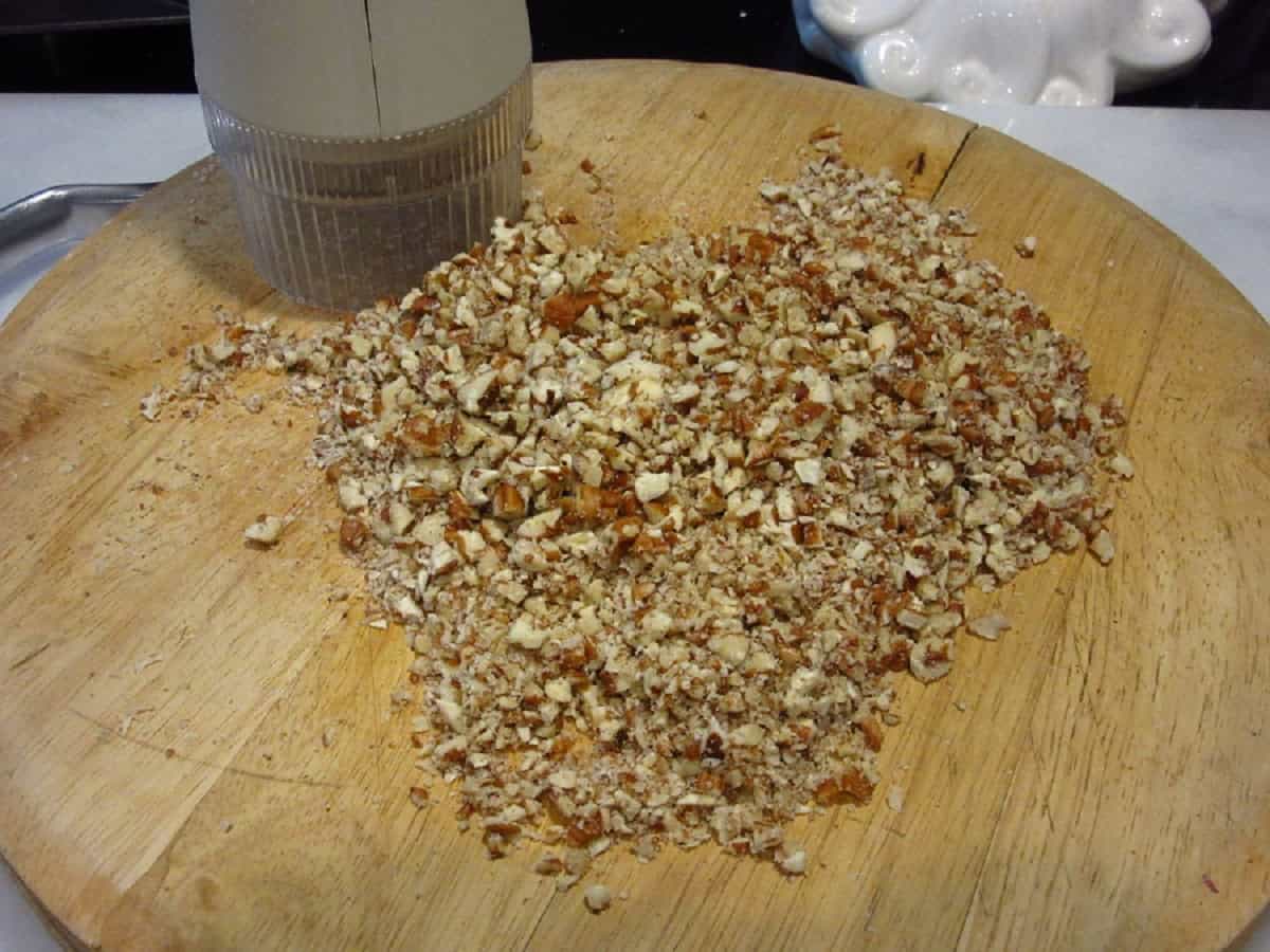 Chopped pecans with a nut chopper on a wooden cutting board.