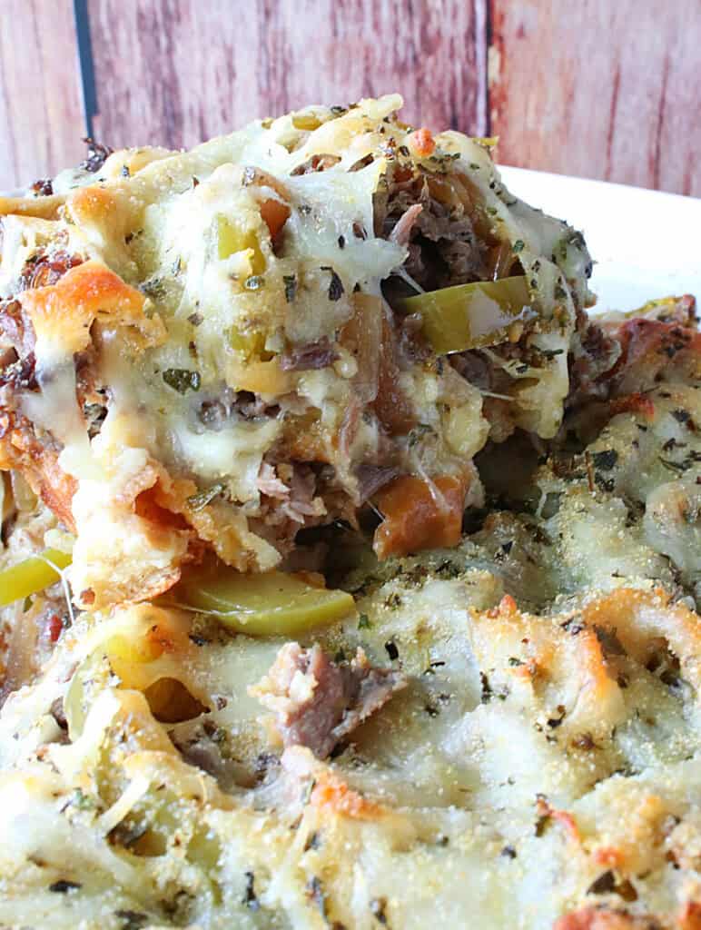 A serving of cheesy beef bread pudding being lifted from a casserole dish.