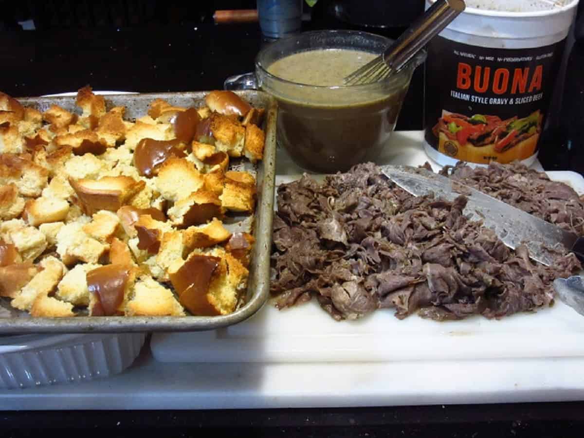 Toasted bread on a baking sheet and chopped Italian beef on a cutting board.