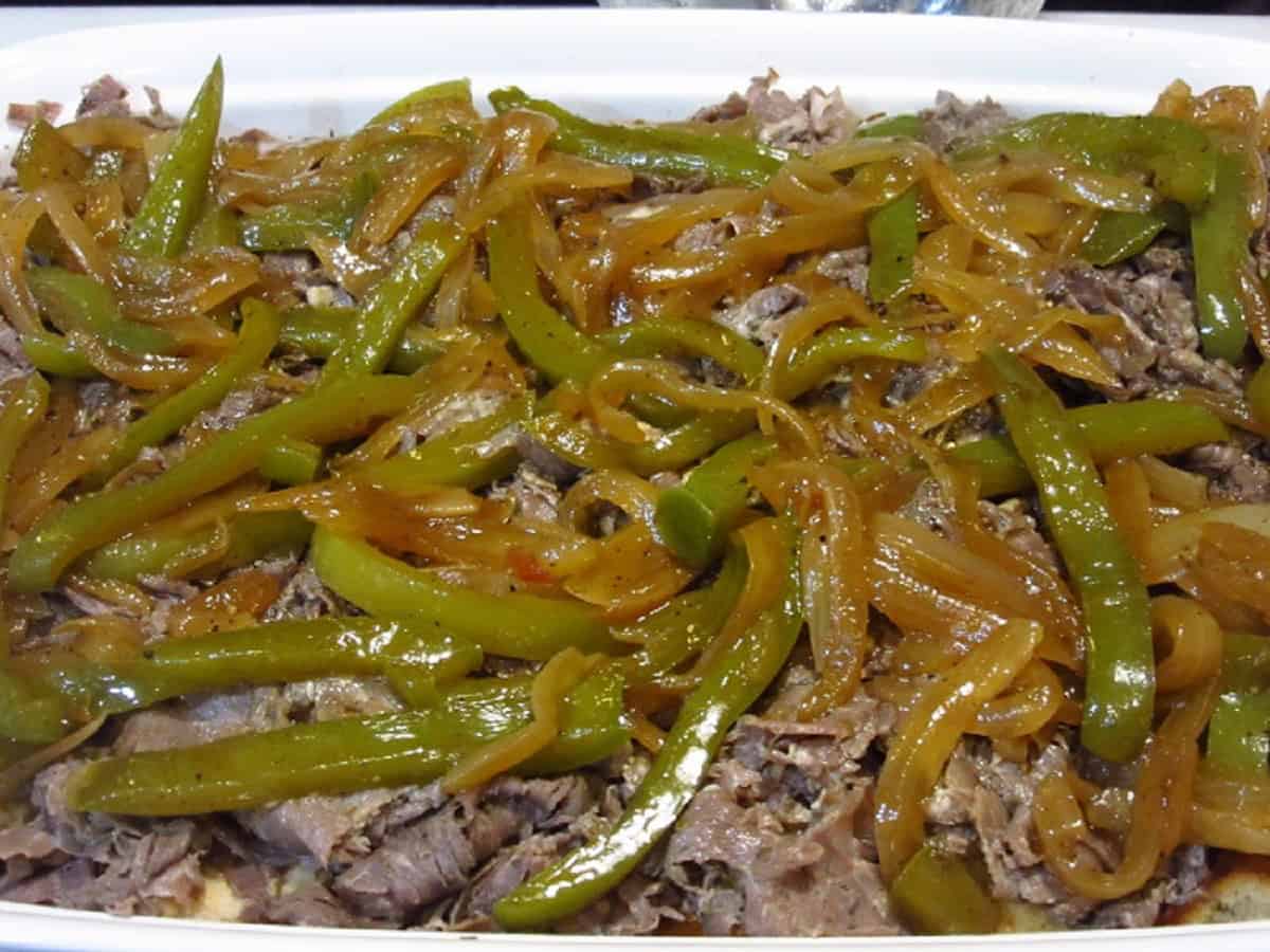 Cooked peppers and onions on top of Italian beef in a casserole dish.