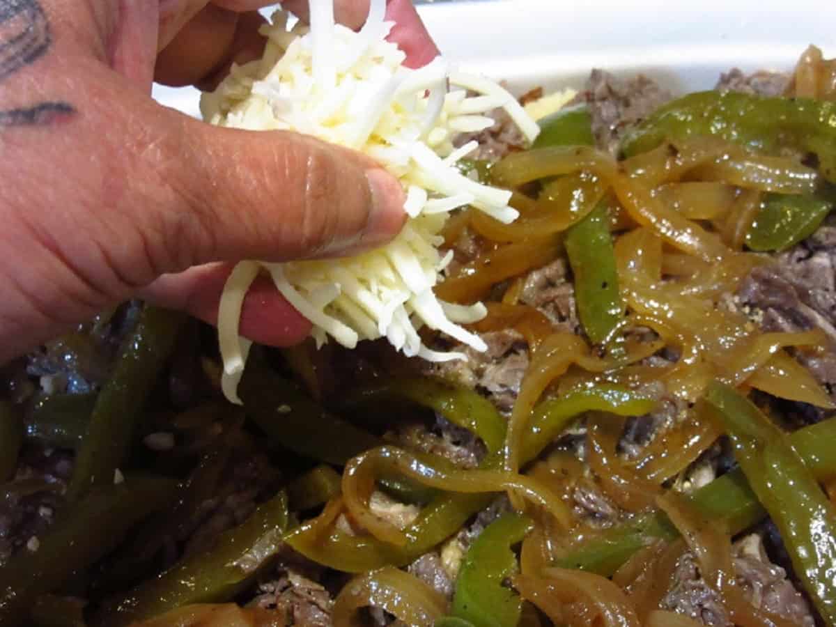 A hand sprinkling cheese over peppers and onions in a casserole dish.